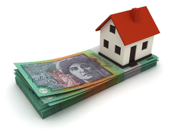 Toy-sized house sitting on top of money.