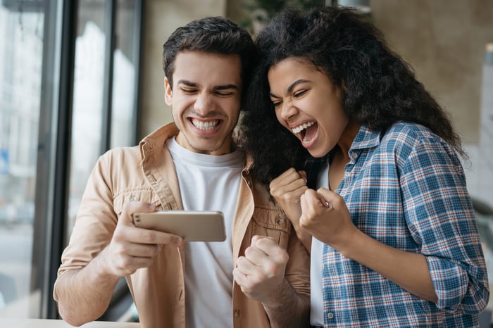 Two people cheering while looking at a cellphone.