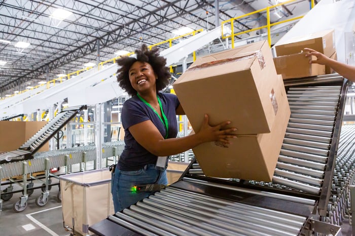 A person smiles while taking packages off of a conveyer belt. 