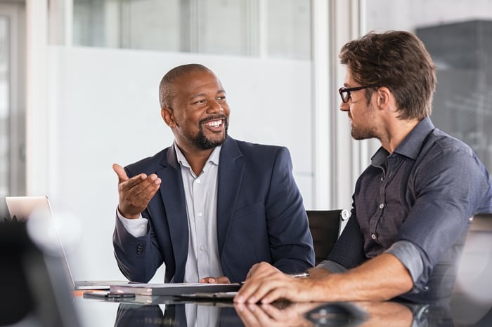 A person smiling while talking to another person in a professional setting.