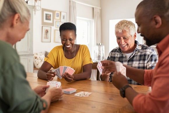 Four people sitting at a table and playing a card game.