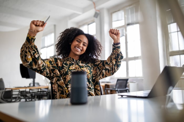 An investor sits at a laptop in an office and cheers.