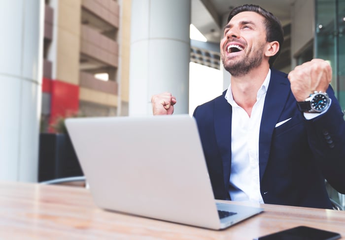 An investor cheers in front of a laptop.