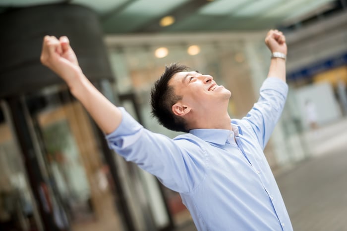 An investor looks up at the sky and cheers on a city sidewalk.