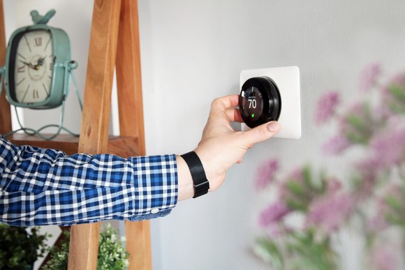 A person adjusts a thermostat in a home.