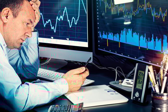 A money manager analyzing stock charts and volume data displayed on two computer monitors.