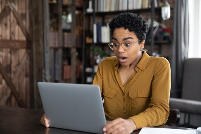 A person looks surprised while sitting in front of a laptop computer.