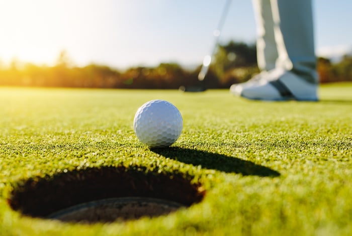 A golf ball rolls toward a cup on a golf course's finely cut green.