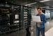 man holds computer in a room full of computing infrastructure