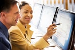 two business people smile while looking at computer data