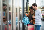 Two people wondow shopping and holding shopping bags in a strip outdoor mall