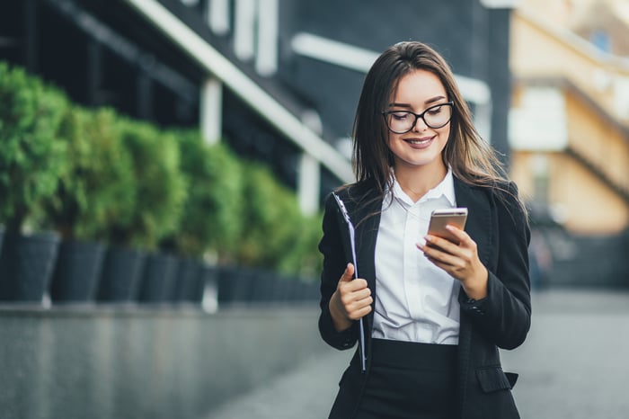 An investor smiles while walking outdoors and looking at a phone.