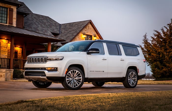 A white 2024 Jeep Grand Wagoneer, a large 3-row SUV, in front of a country house.
