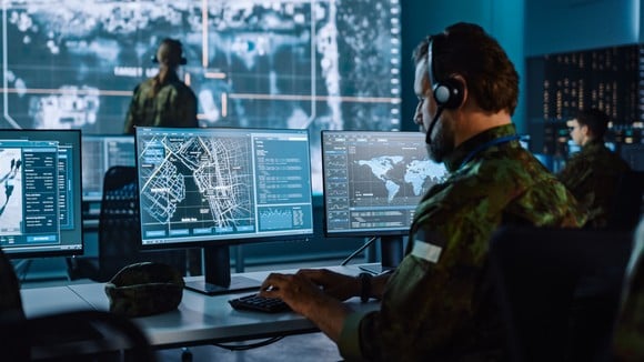 Military personnel in a command center using computers and wall-sized displays.