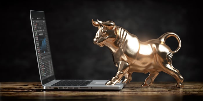 A rendering of a table with a gold bull on top of the table resting on a laptop computer that displays financial information. 