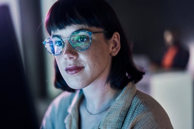 A business person looking at charts on a computer with light reflecting off their glasses