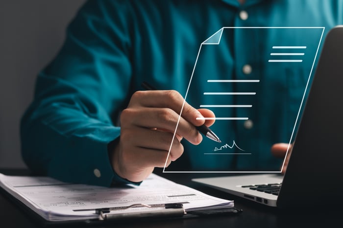 Person signing a document that's floating over a laptop. 