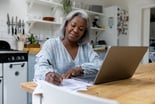 Person in kitchen filling out documents in front of her computer