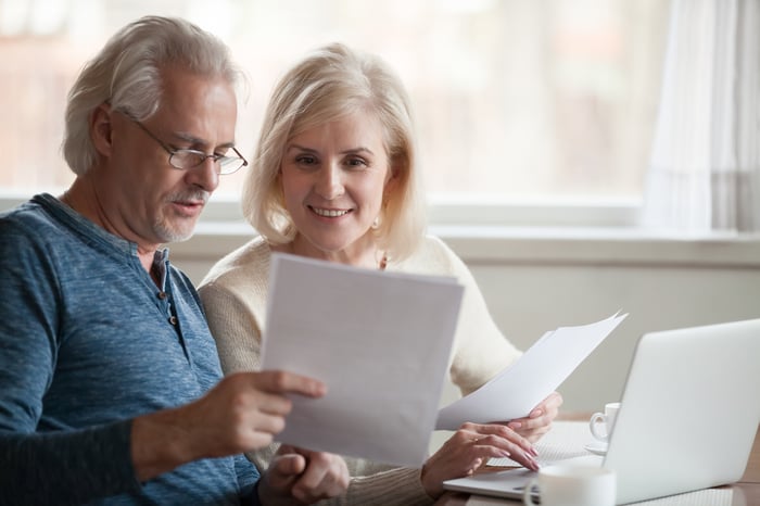 Two people look at paperwork and use a laptop.