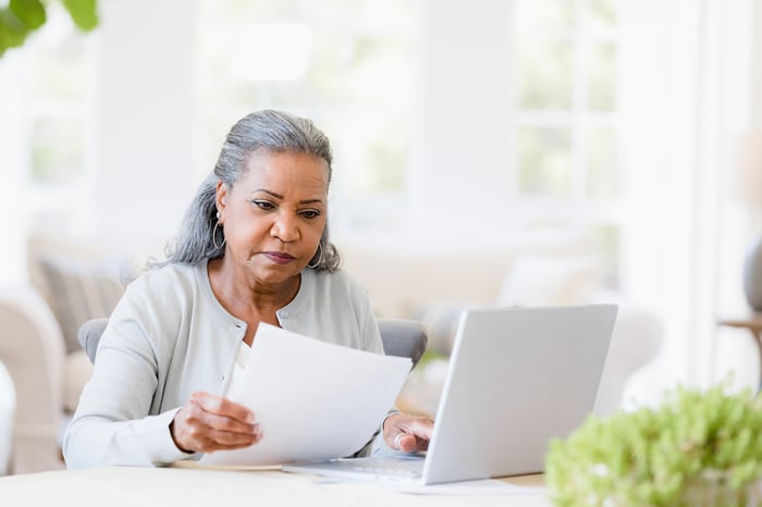 Serious person looking at documents while sitting at laptop.