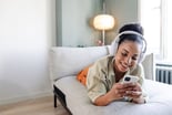 Happy person using headphones and a phone while lying on a couch