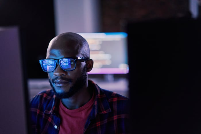 A person sitting in front of a computer with the content on the computer screen reflected on their glasses.