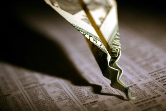 A twenty dollar bill paper airplane that's crashed and crumpled into the business section of a newspaper.