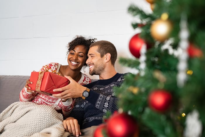 A smiling young couple exchanges Christmas gifts by a Christmas tree.