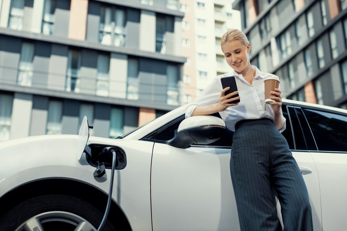 A driver checks a phone while charging an EV.