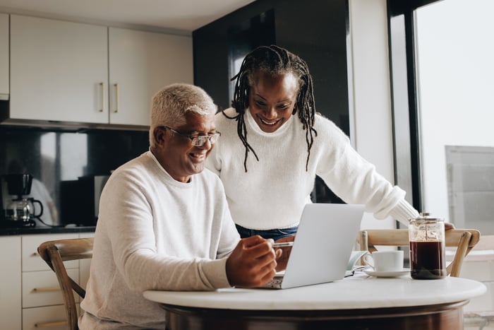 Smiling couple looking at laptop together in kitchen.