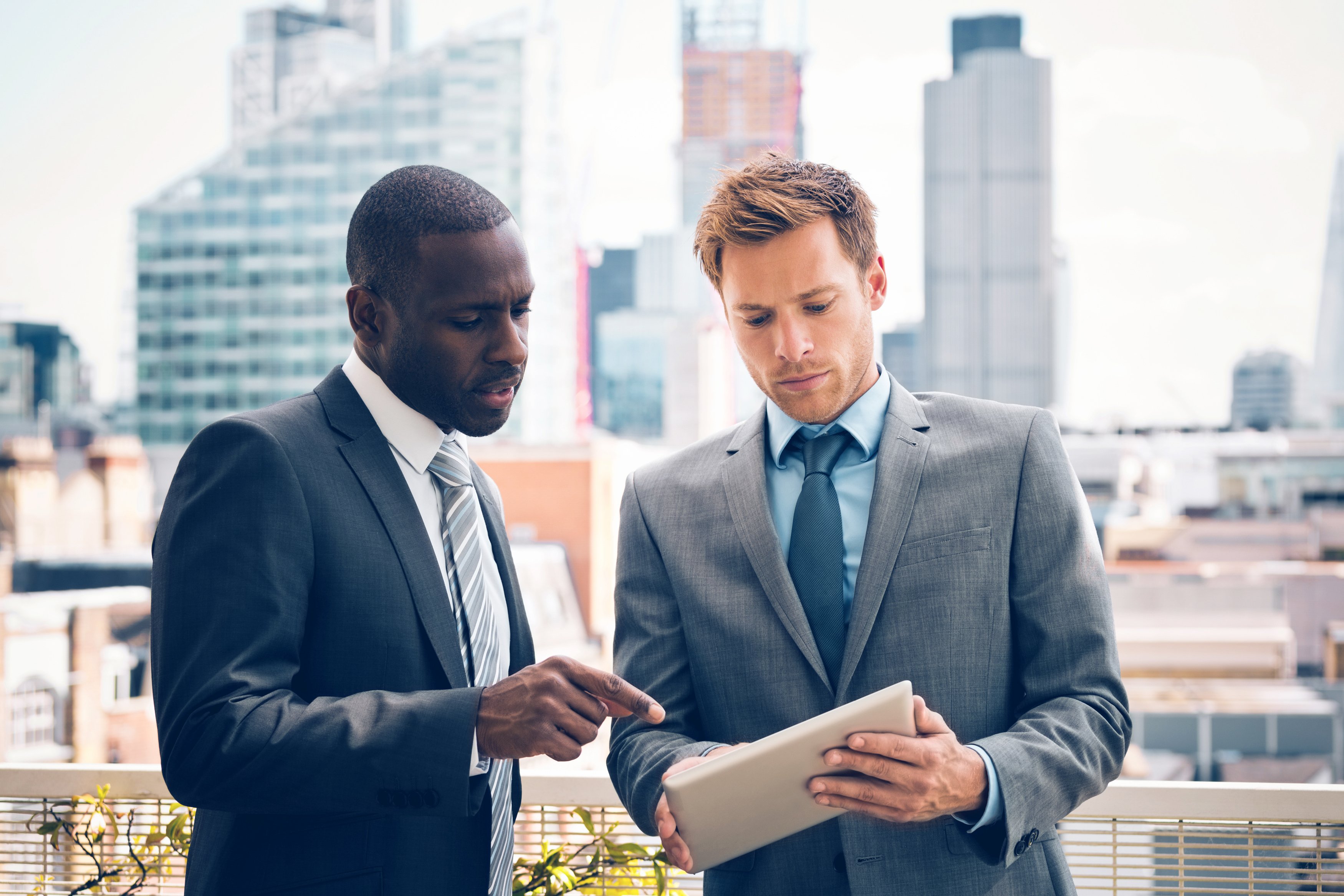 Two people in suits reviewing a document while buildings loom in the background