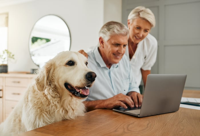 Two people looking at a laptop with a dog sitting beside them.