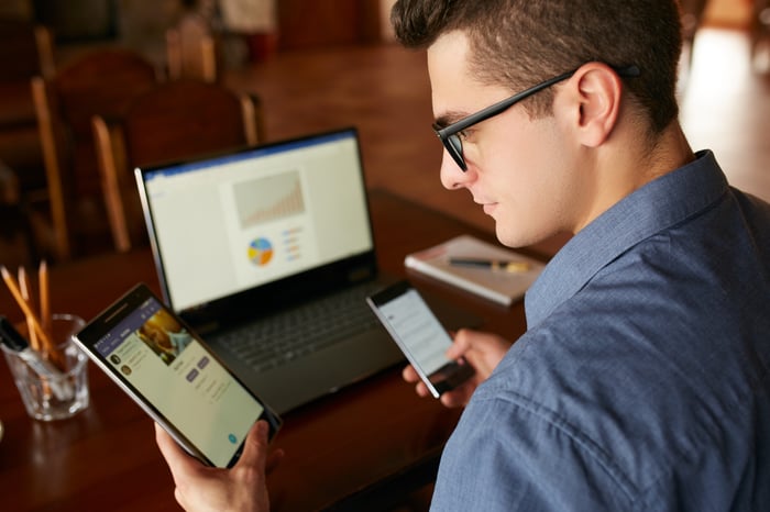 An investor looking at their phone while seated in front of a computer. 
