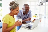 mature man and woman sitting in kitchen looking at laptop computer and smiling -- couple POC