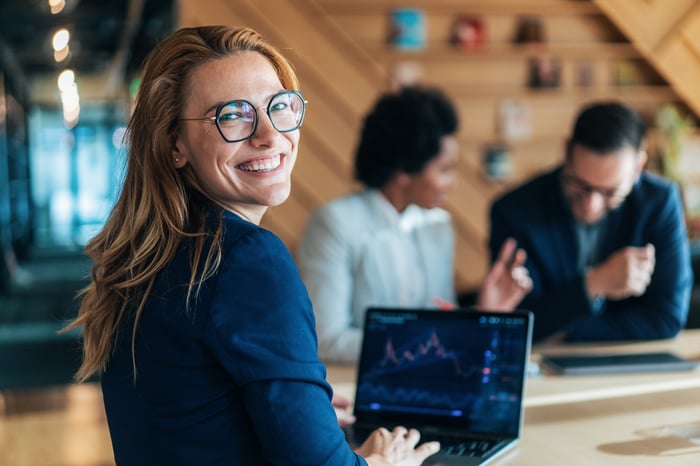 Someone at a laptop is looking back over her shoulder, smiling.