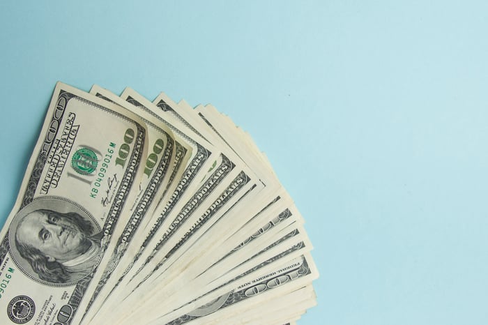 Many $100 bills fanned out on a light blue background.