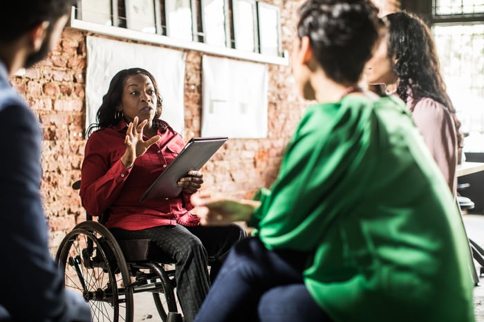 Person leading business meeting and holding tablet.