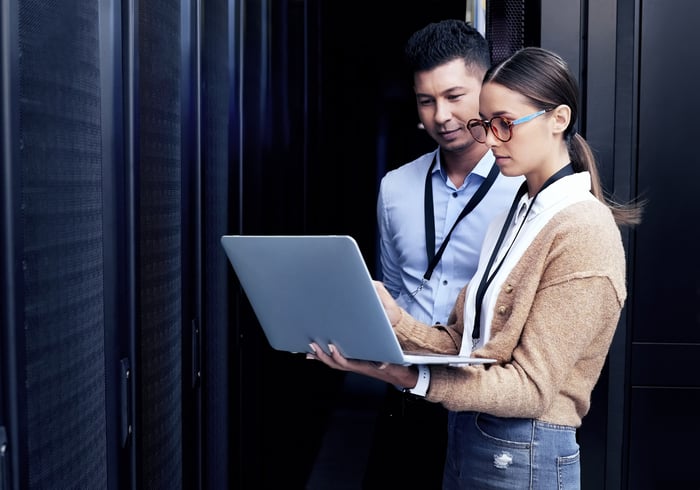 Two people standing inside a data center looking at a laptop computer.