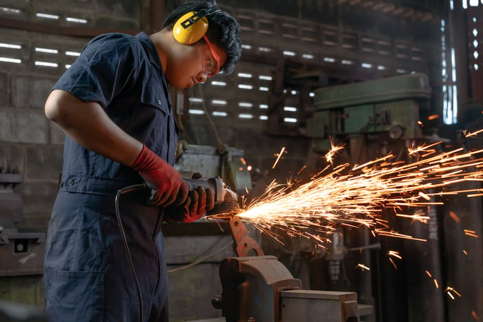 Sparks fly as a person wearing personal protective equipment uses a power tool in an industrial setting.