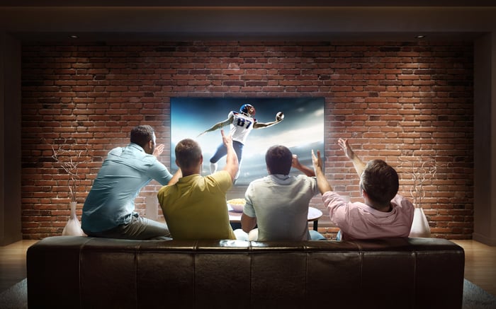 Four people cheering on touchdown celebration on TV from the couch.