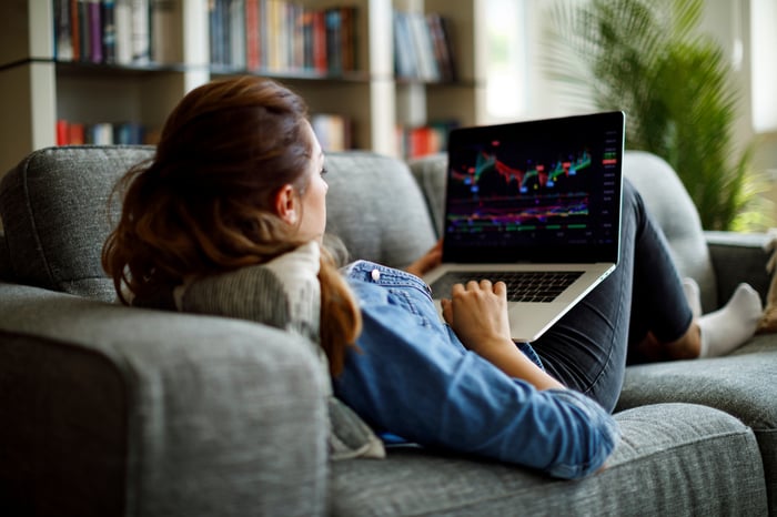 Person lying on couch, looking at stock chart on laptop.