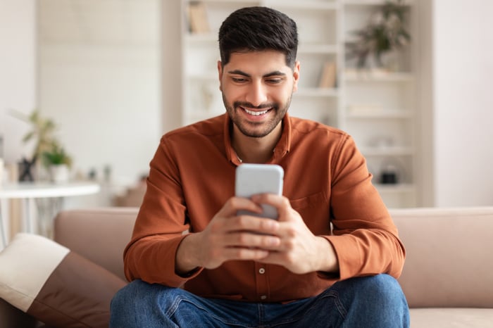 An investor smiles while looking at a phone in a living room.