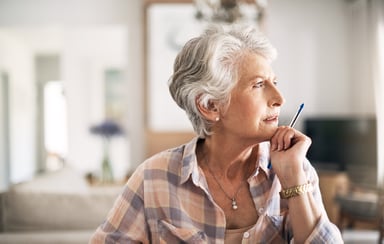 older person looking thoughtful while holding a pen