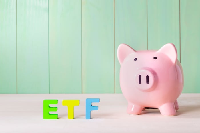 A pink piggybank placed next to colored wooden blocks that spell ETF.
