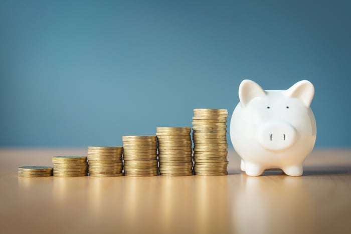 A piggy bank next to increasingly taller stacks of gold coins.