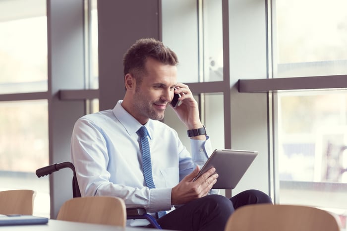 An investor talks on the phone while looking at a tablet.