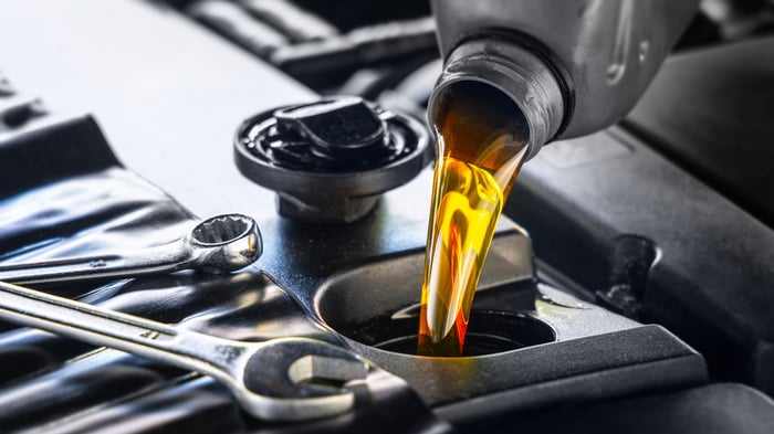 A cap is removed and motor oil is poured into an oil fill port.