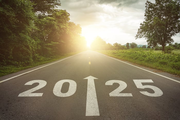 A street has 2025 and an arrow painted in white on the pavement and pointing up the road toward the sun. 