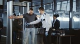TSA agent wanding a passenger at an airport x-ray machine.