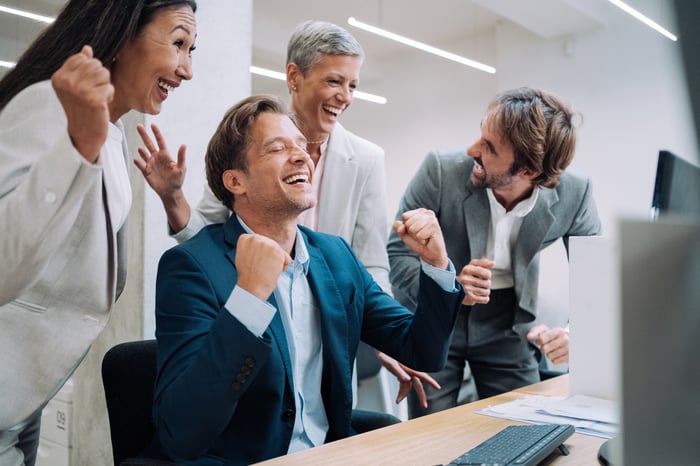 A group of investors cheer in front of a computer in an office.